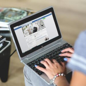 A woman typing on a laptop with social media on the screen, indoors setting.